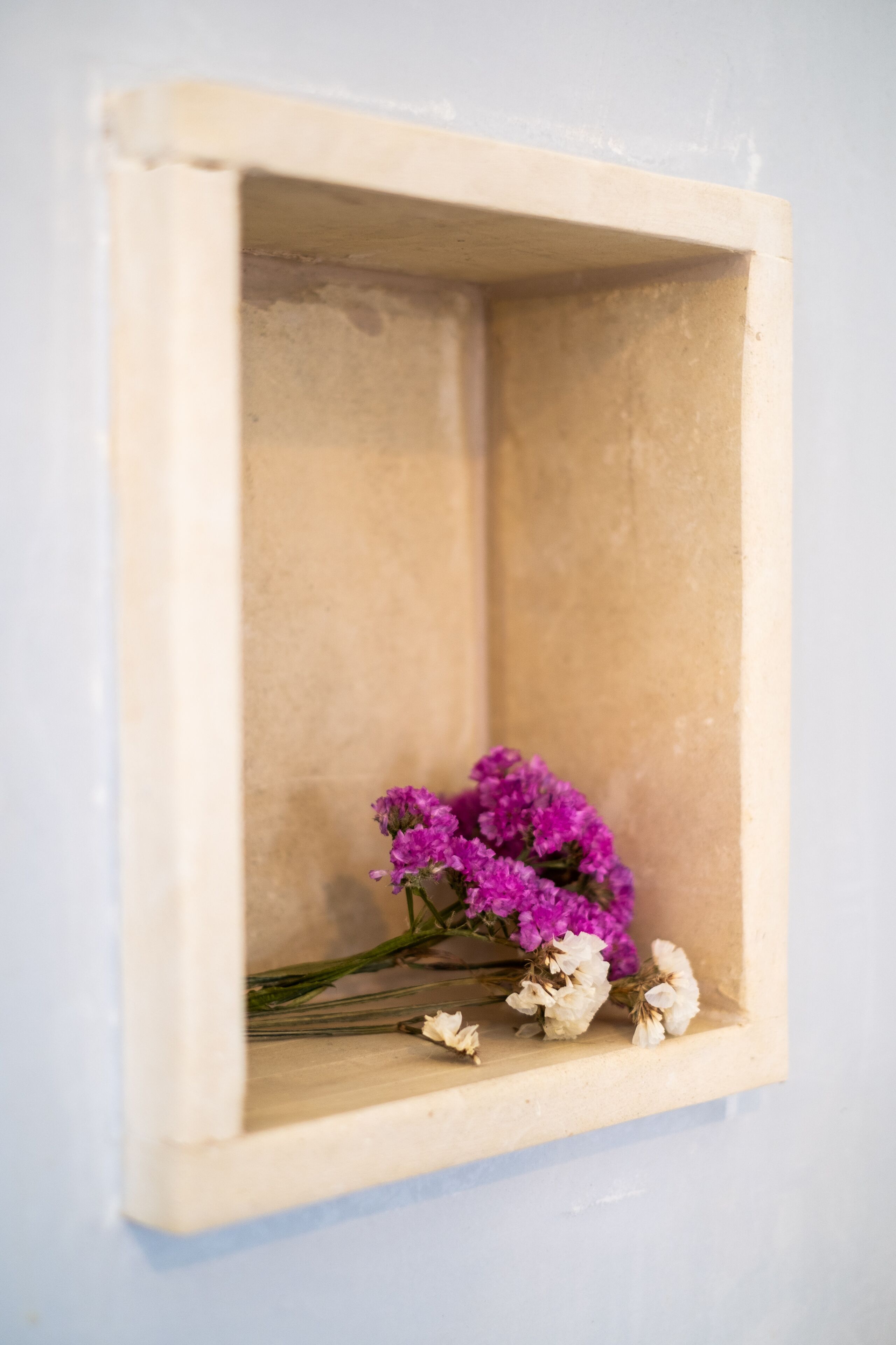 A small, empty, beige-framed shelf against a light blue wall.