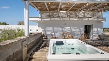 Un jacuzzi bajo una pérgola de madera, con una pared exterior blanca y una puerta.