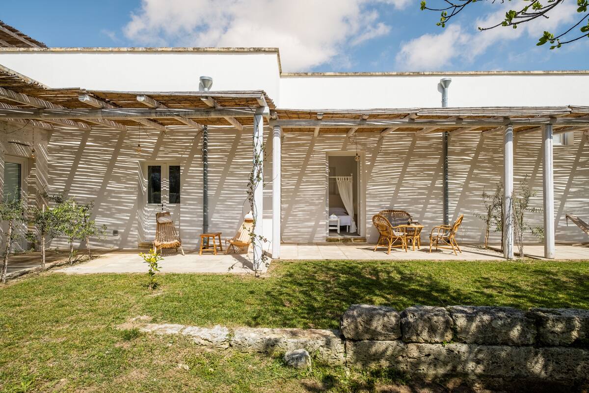 Eine überdachte Terrasse mit Pergola, Sitzgelegenheit und kleinem Garten.