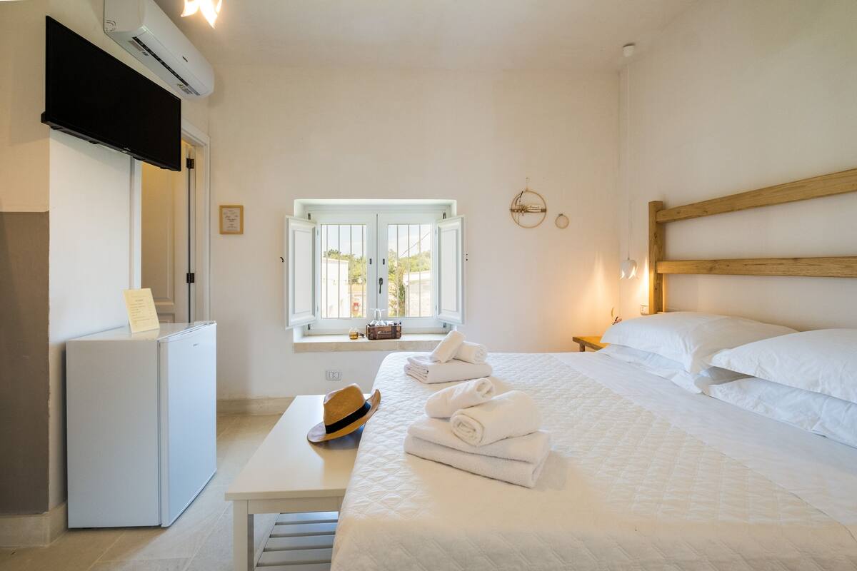 Ein Hotelzimmer mit Bett, Schreibtisch, Kühlschrank, Fenster und einem Wand-Fernseher.