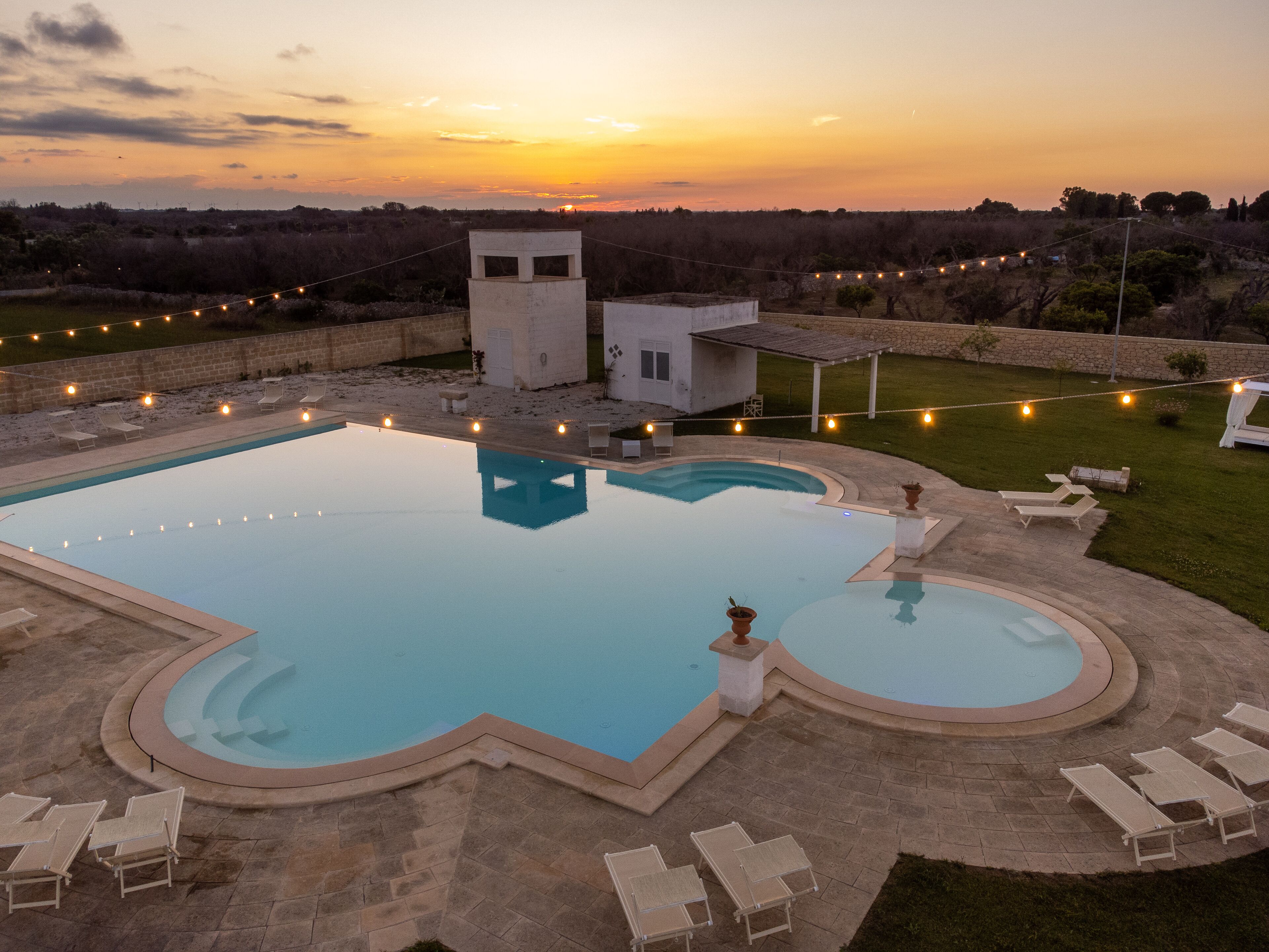 A rectangular swimming pool with a small adjacent pool, surrounded by lounge chairs and a stone deck.