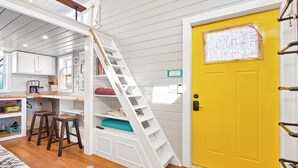 Een compacte, meerlaagse kamer met een houten trap, een gele deur en een kitchenette.