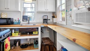Een keuken met witte kastjes, een houten aanrecht, een fornuis, een gootsteen en een raam met uitzicht op buiten.