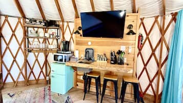 A compact kitchen with a microwave, coffee maker, and wooden shelves.