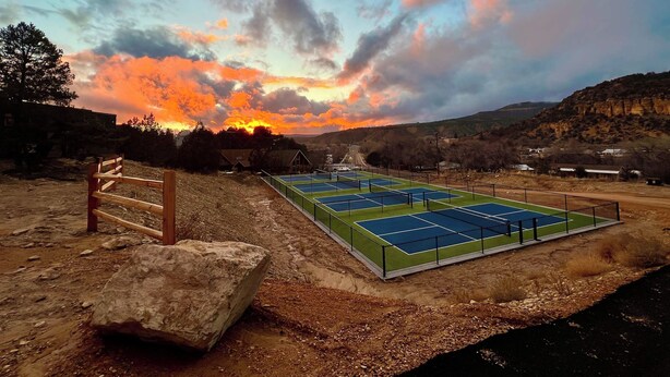 A tennis court with a wooden fence and a large rock nearby. - Glamping Yurt near Zion with 2 King Beds & Views (Orderville)