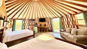 A yurt interior with a central octagonal skylight, two beds, a sofa, a dining area, and a TV. - Yurt Overlook #10 with AC and Private Bath 2 Kings (Orderville)