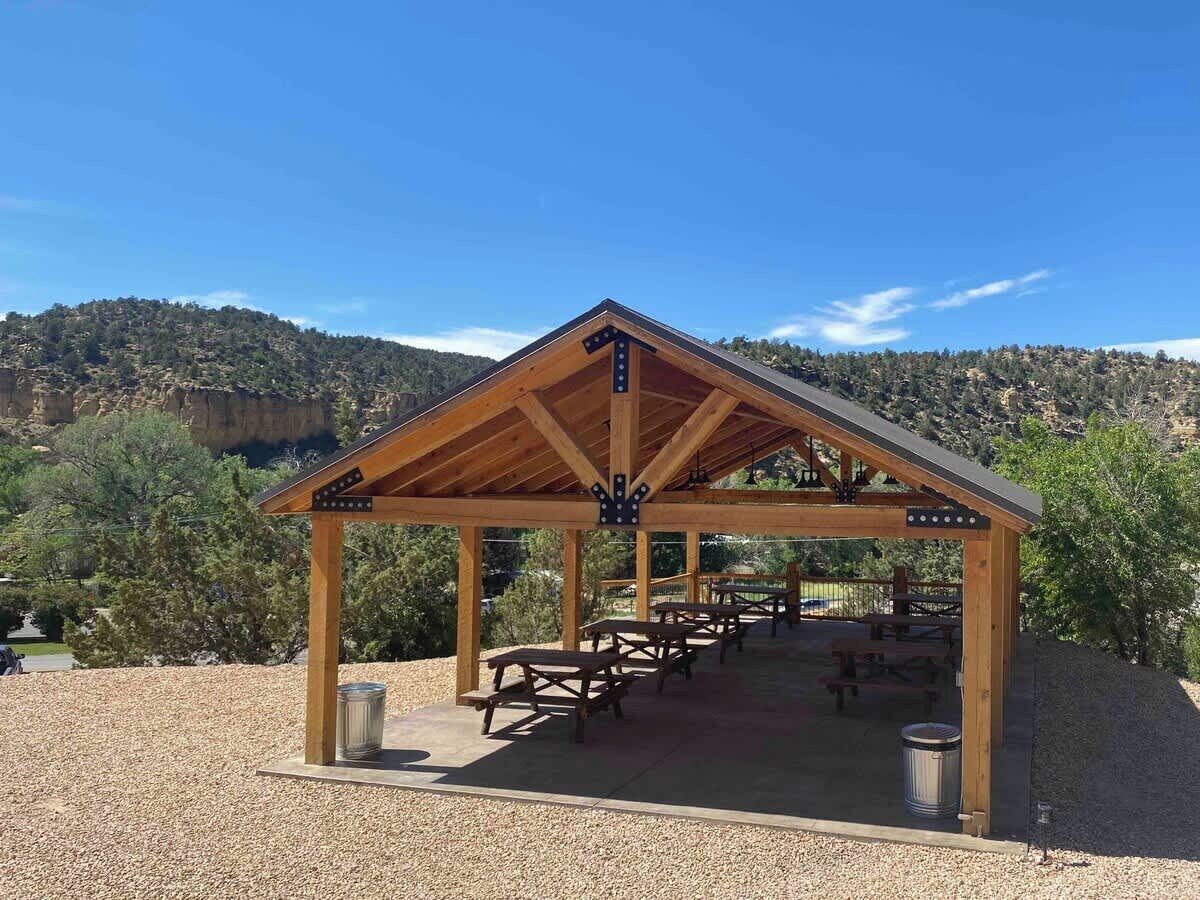A wooden pavilion with picnic tables and trash bins, set against a mountainous backdrop.