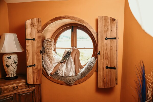 Una habitación acogedora con un ventanal de madera circular, una lámpara blanca y un jarrón decorativo.