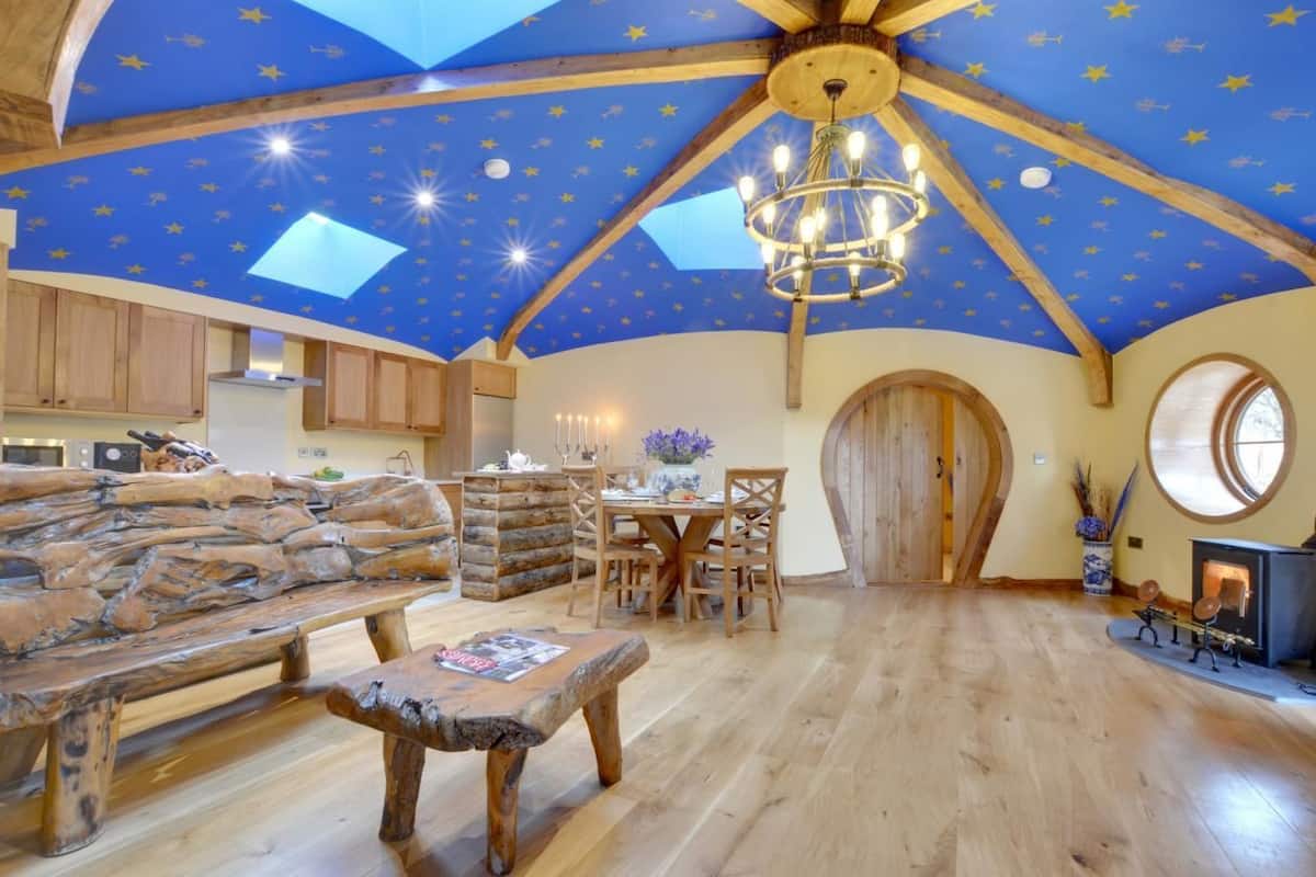 A rustic interior with a wooden ceiling, a stone fireplace, and a dining area.