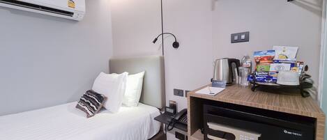 Een hotelkamer met een bed, een nachtkastje met een waterkoker, een koffieapparaat en een minibar.