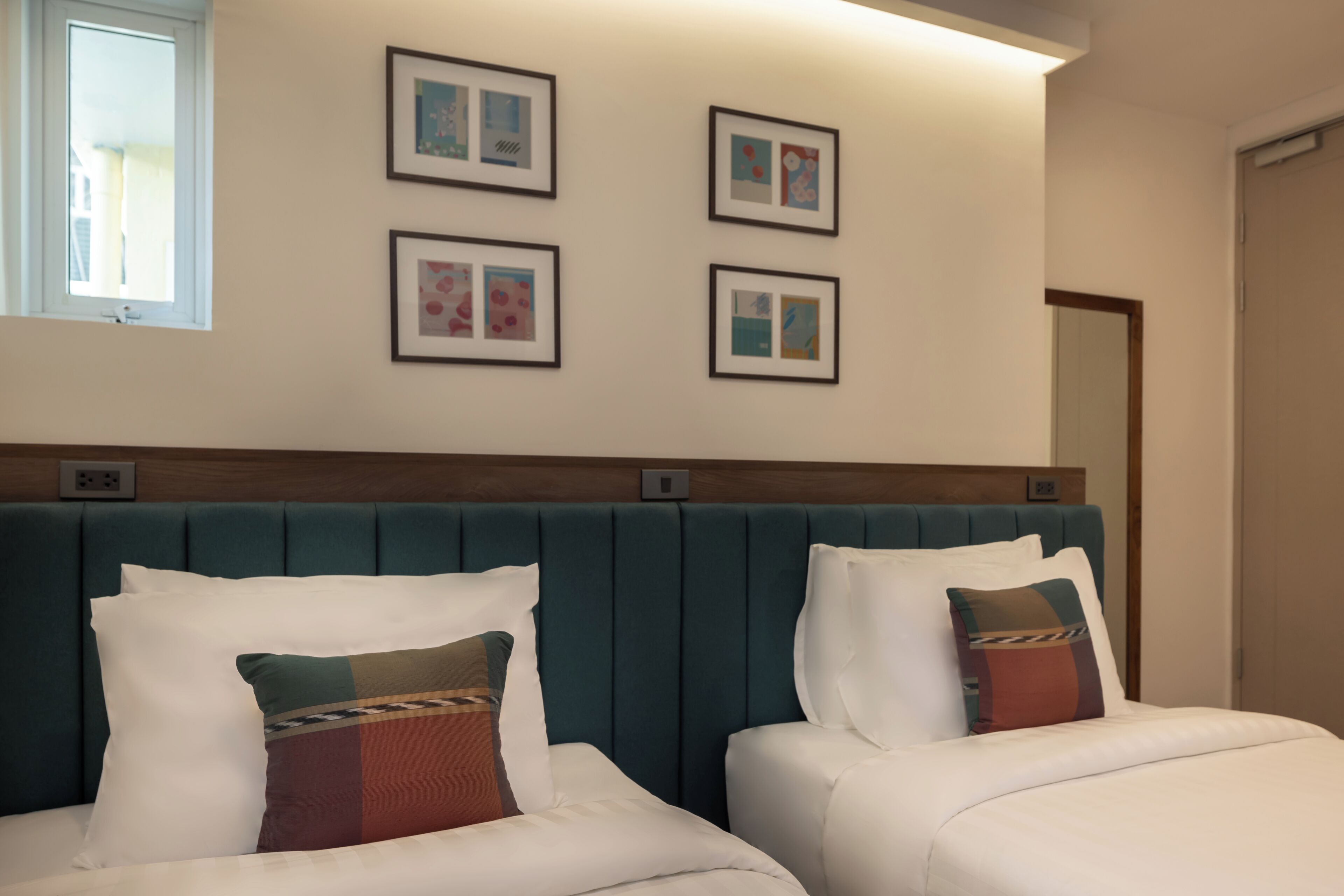 Habitación de hotel con dos camas, cabecero y cuatro cuadros en la pared.