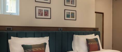 Habitación de hotel con dos camas, cabecero y cuatro cuadros en la pared.