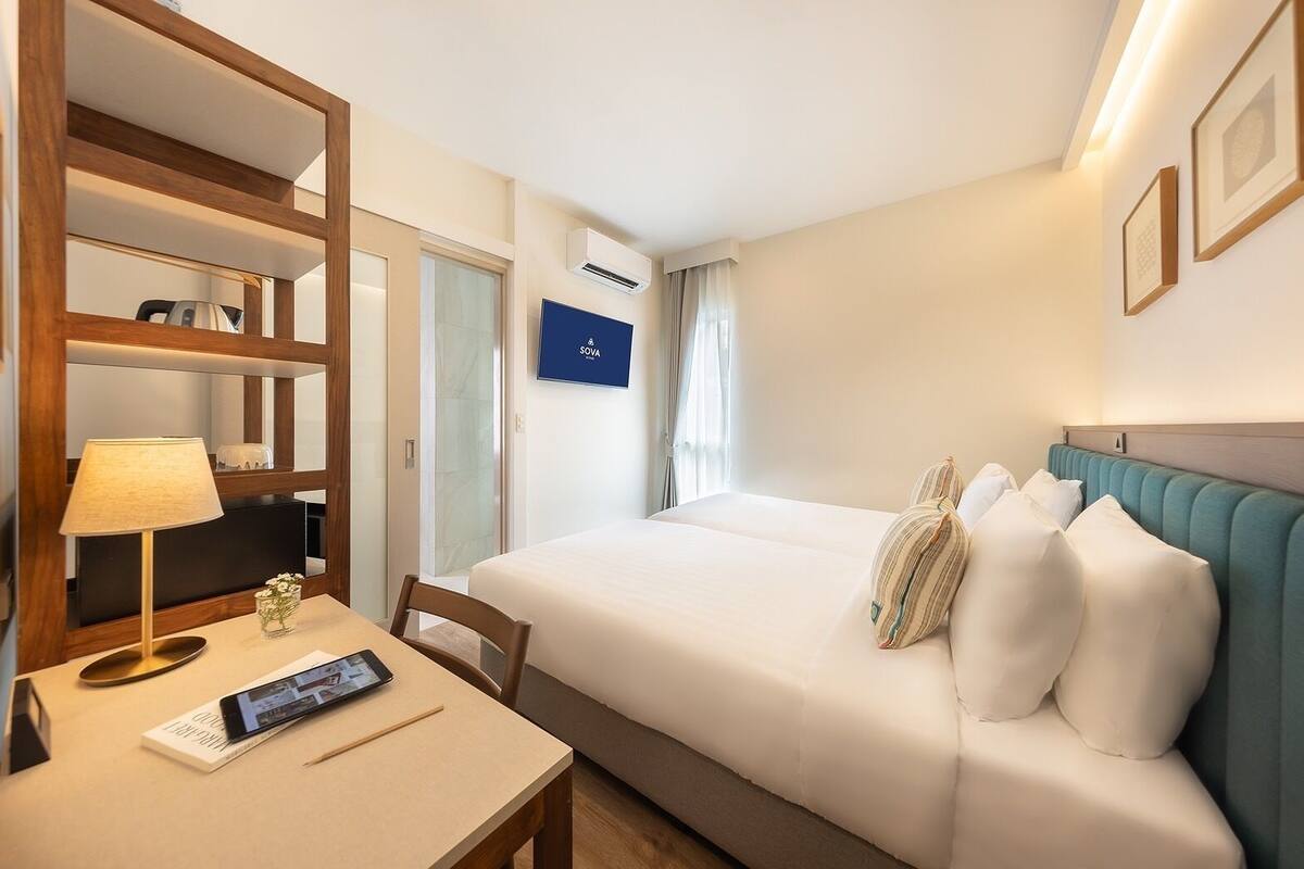 A hotel room with a bed, a desk with a lamp, a chair, a TV, and a wardrobe.