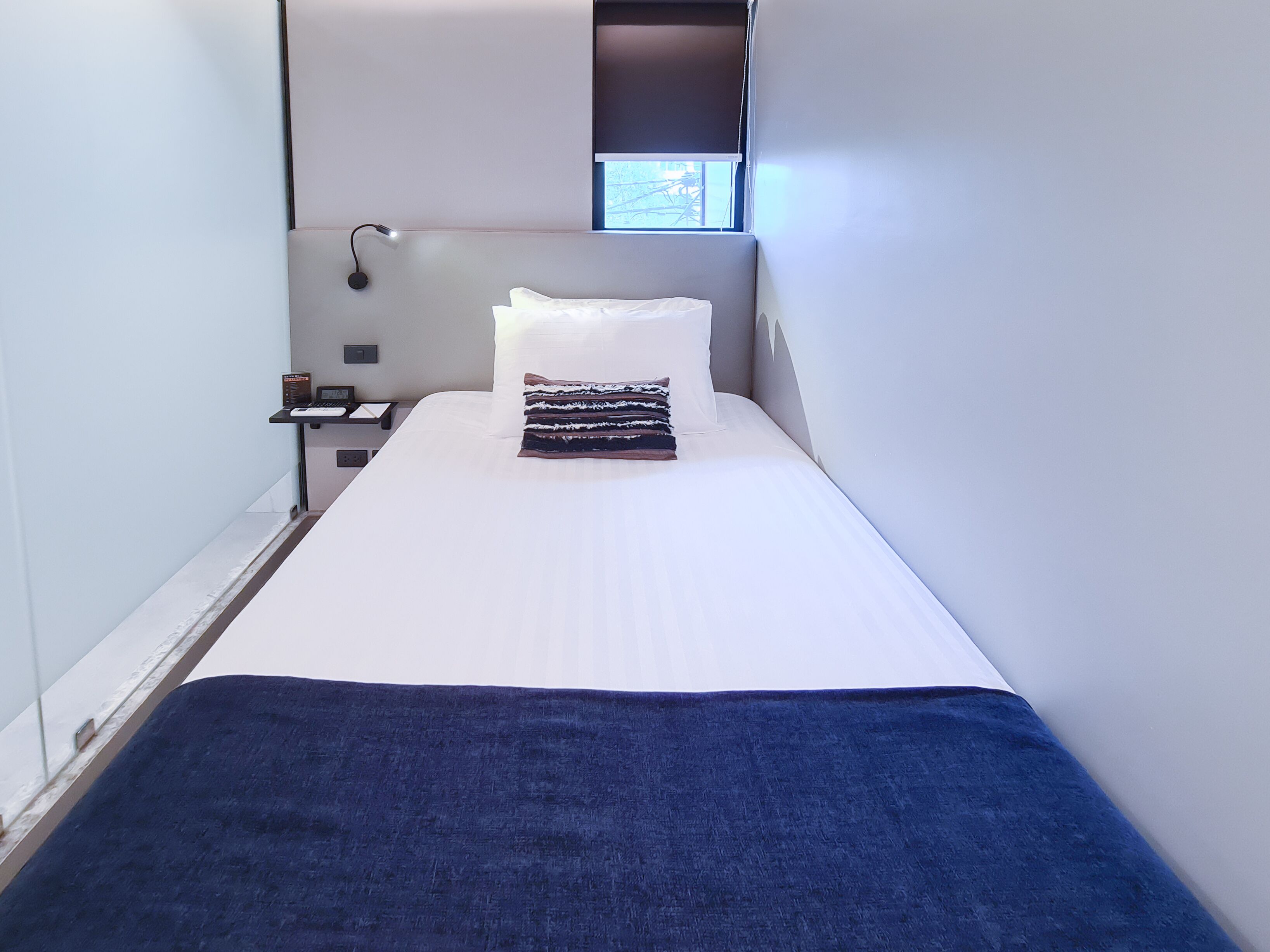 A modern hotel room with a single bed, a bedside table, a lamp, and a window with a view.