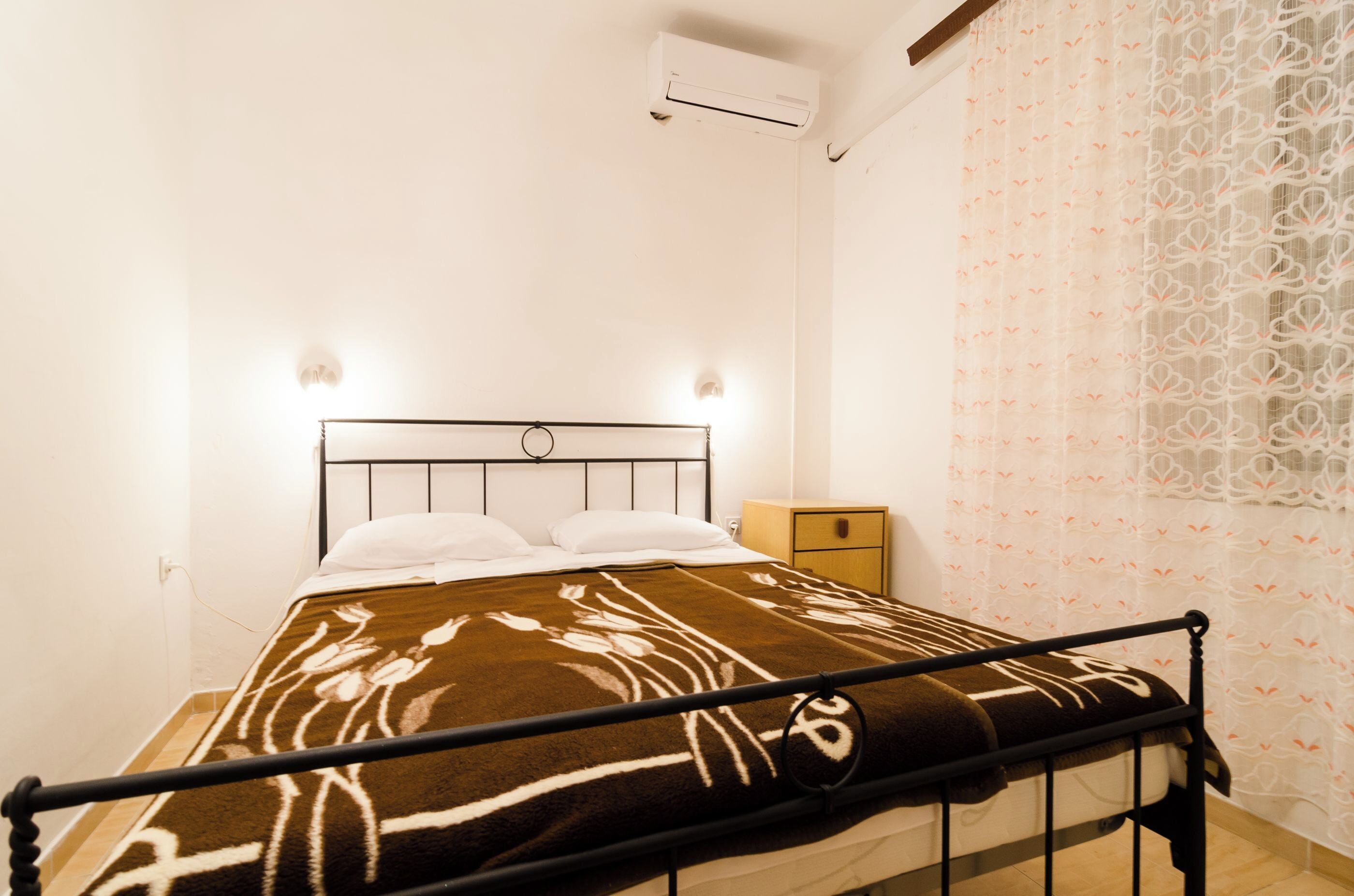 A single bed with a headboard, a bedside table, and a wall-mounted air conditioner.