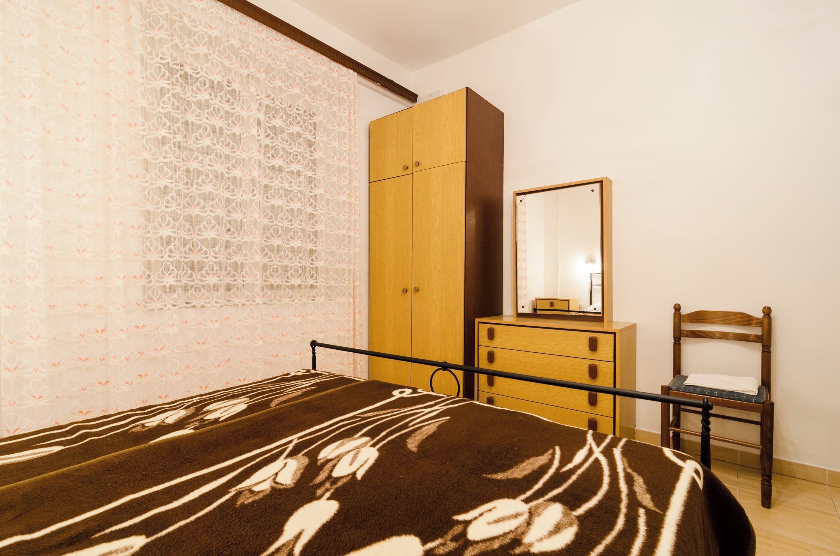 Un dormitorio con cama, armario, silla y espejo.