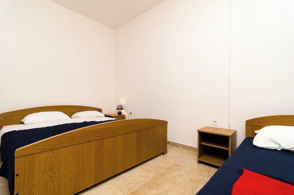 A bedroom with two wooden beds, a nightstand with a lamp, and a small wooden shelf. - Guest House Kiko (Mljet)