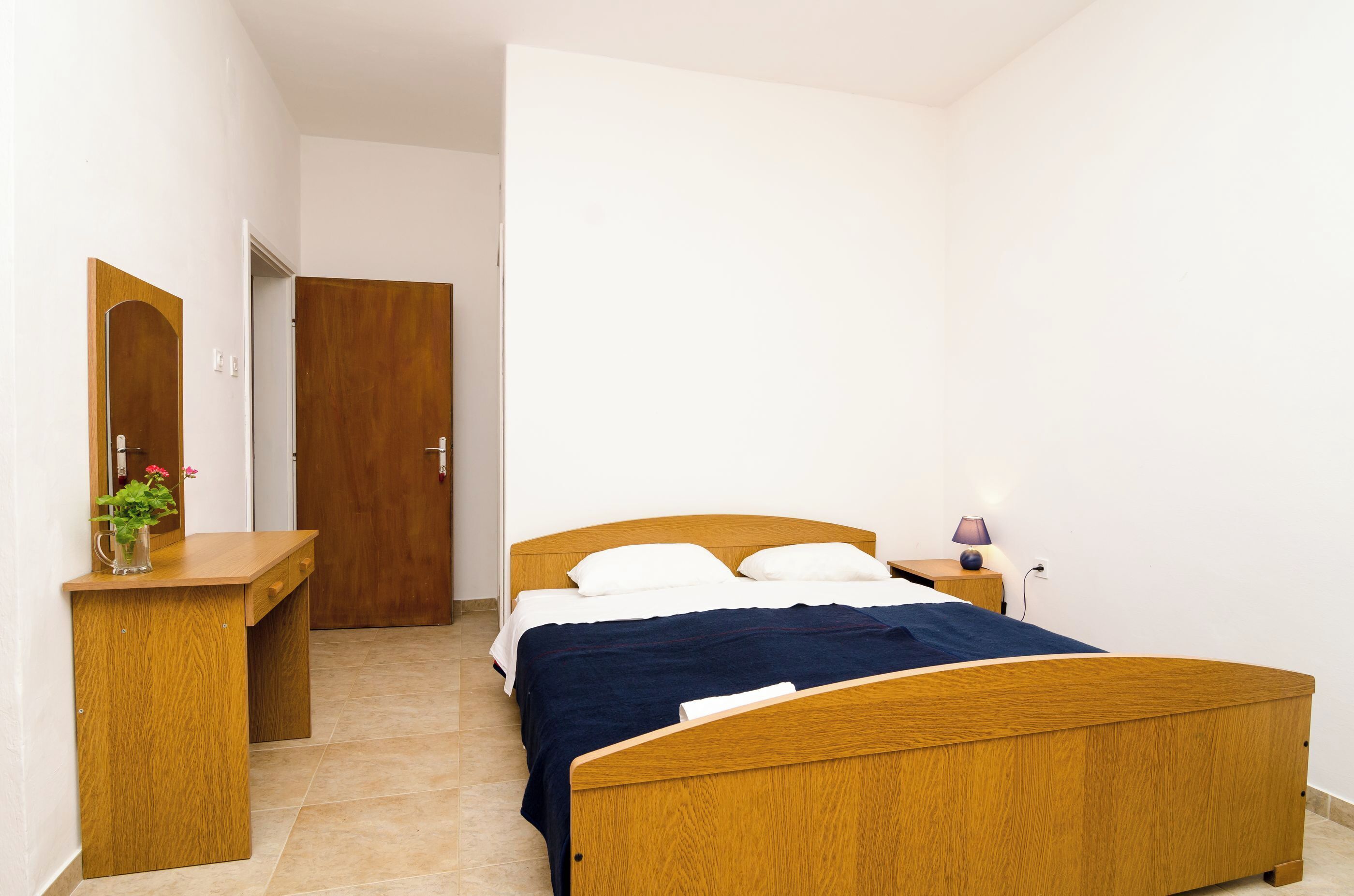 A bedroom with a wooden bed, a bedside table, a nightstand, and a mirror.