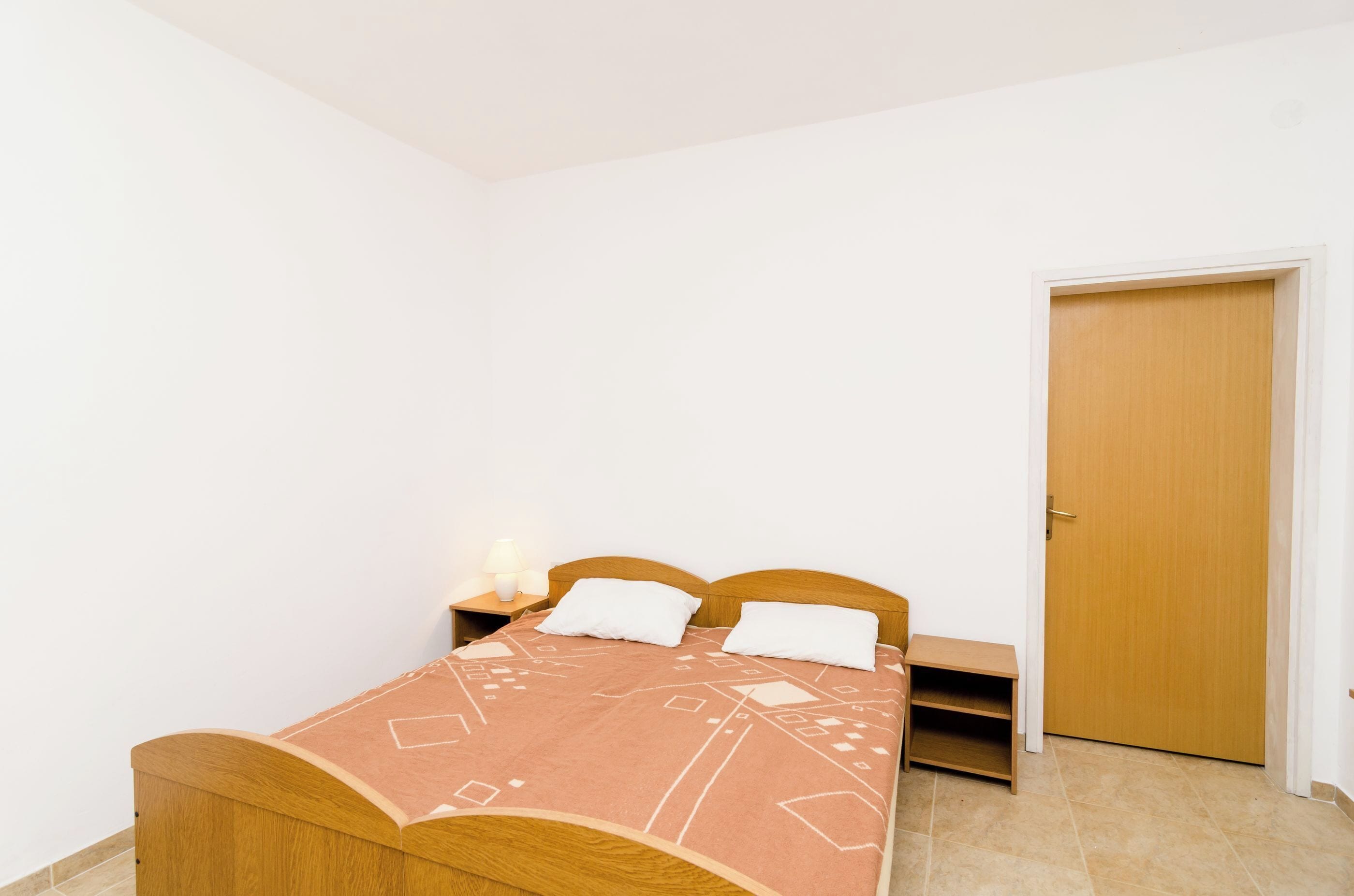 Un dormitorio pequeño y ordenado con una cama individual, una mesita de noche con lámpara y una puerta.