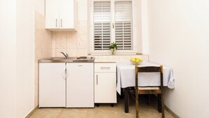Una cocina compacta con muebles blancos, una estufa empotrada y una ventana con contraventanas.