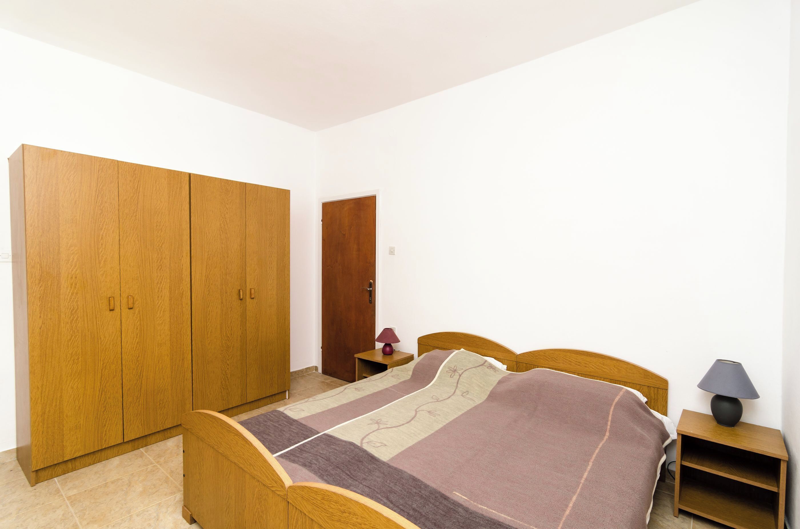 Ein Schlafzimmer mit einem hölzernen Bett, einem Nachttisch, einem Kleiderschrank und einer Tür.