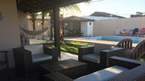A covered outdoor seating area with wicker furniture and a pool in the background.