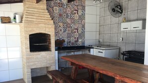 A kitchen with a brick oven, tiled backsplash, wooden table, and bench.