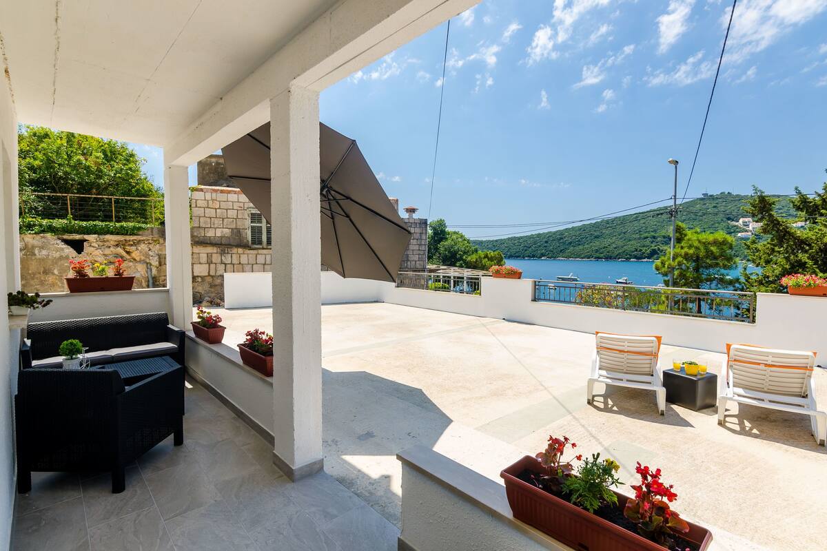 A covered outdoor seating area with a view of the sea, a stone wall, and potted plants.