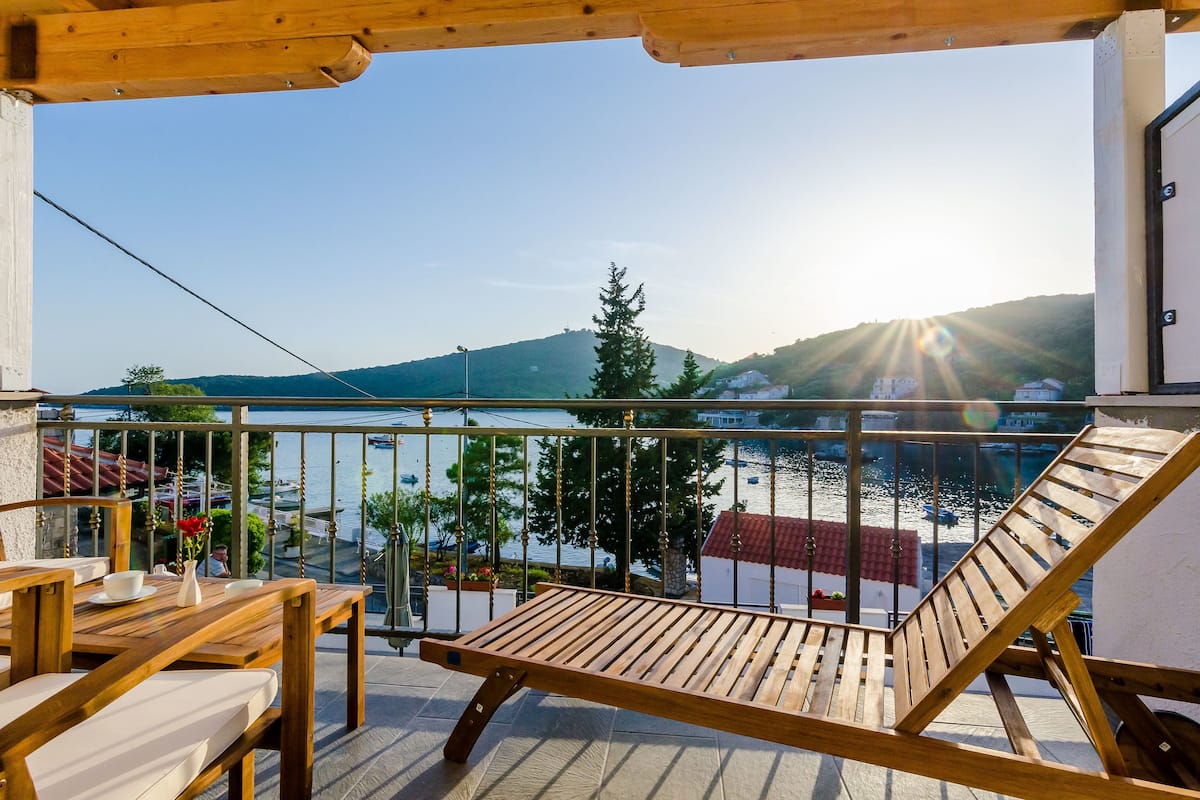 A wooden deck with a view of a lake and mountains, a swing, and a table with chairs.