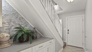 A staircase with white railings leading to a door, a potted plant on the landing, and a tiled floor.