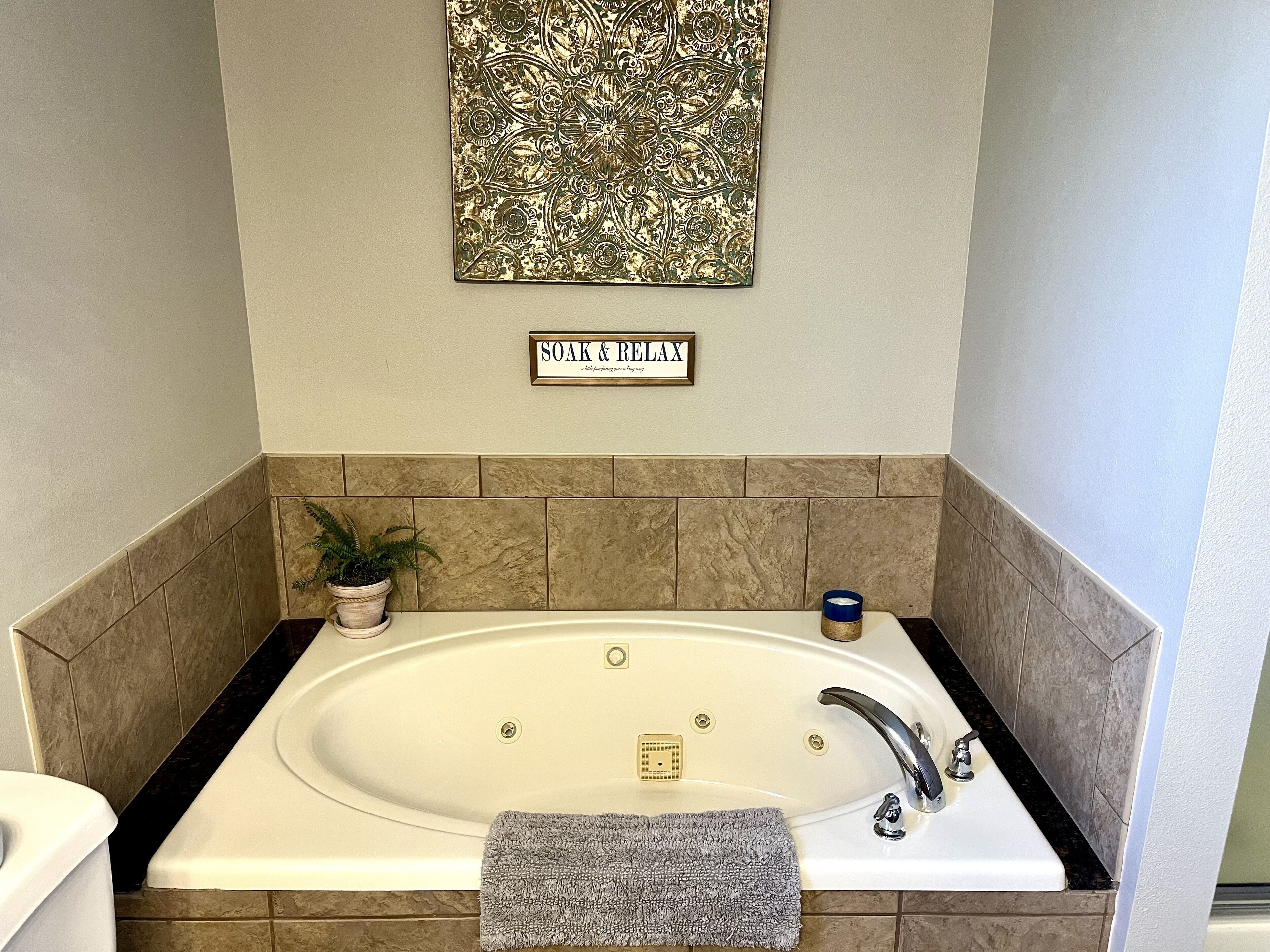 Un baño con bañera, lavamanos, toalla, planta en maceta y un letrero que dice "SOAK & RELAX".