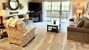 A living room with two sofas, a coffee table, a fireplace, a TV, and a large window with a 'gather' sign.