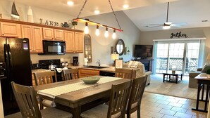 A modern kitchen with wooden cabinets, a black refrigerator, and a dining area with a large table and chairs.