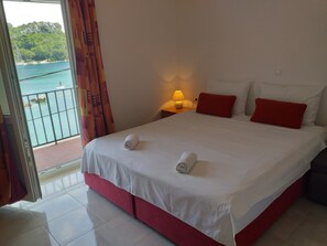A hotel room with a bed, a nightstand, a lamp, and a view of a body of water through a window. - Apartments Paolo (Mljet)