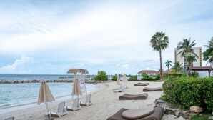 Ett semesterhotell vid stranden med solstolar, parasoller och en pool.
