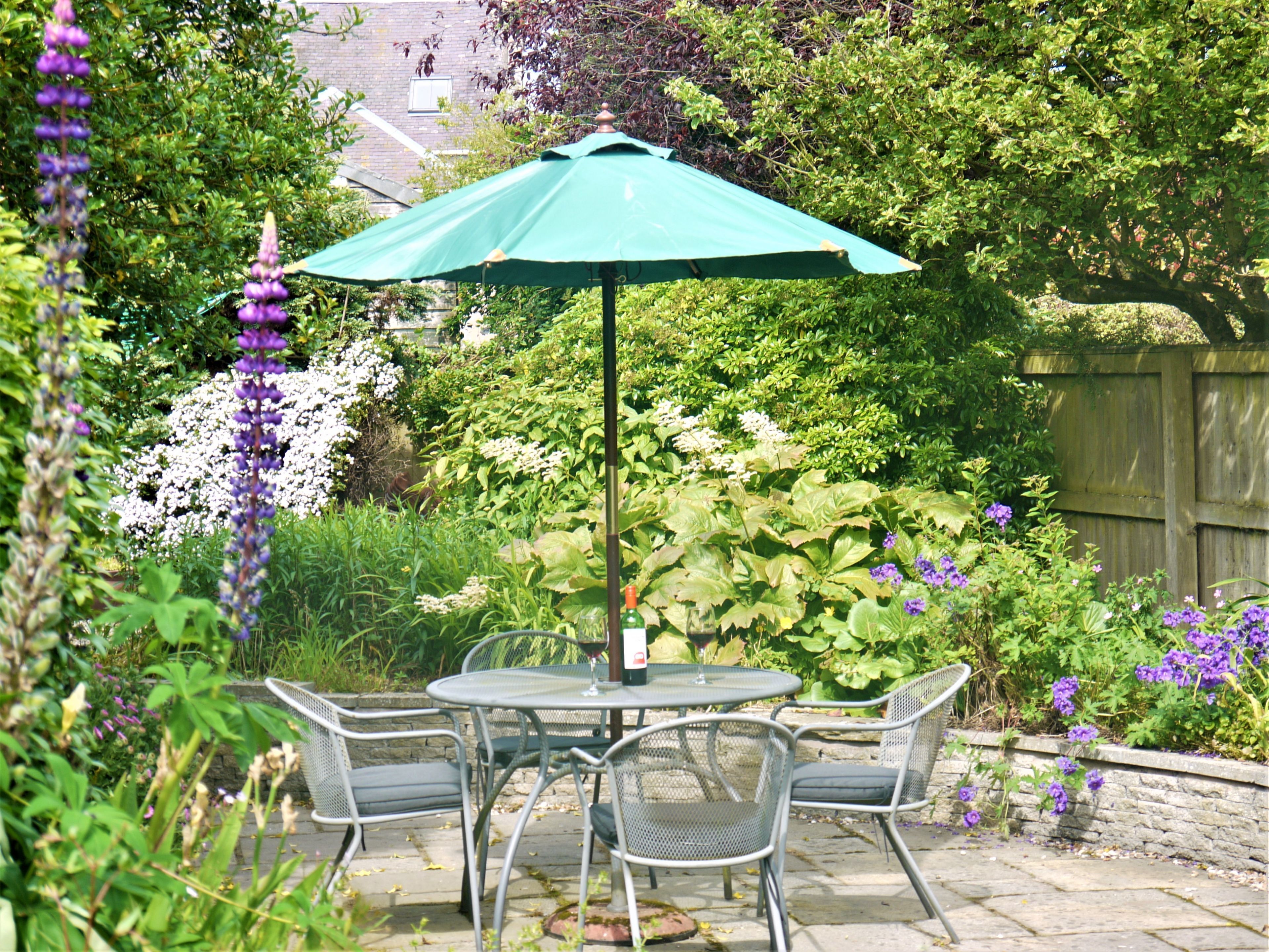 Een terras met tafel en stoelen, omringd door weelderige beplanting en bloeiende planten.