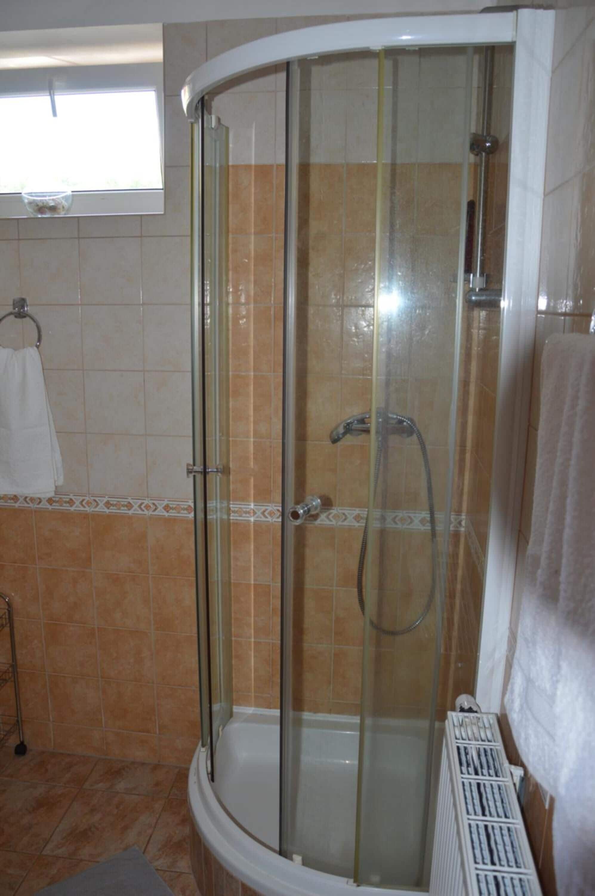 A glass-enclosed shower stall with a handheld showerhead and a wall-mounted faucet.