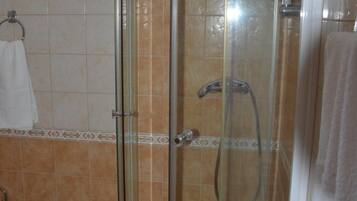 A glass-enclosed shower stall with a handheld showerhead and a wall-mounted faucet.