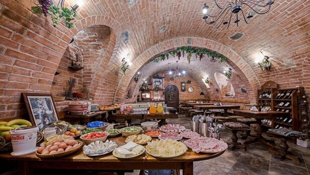 A restaurant with brick arches, a variety of food items on display, and a wine rack. - Apartmány Divoký anděl (Dolní Moravice)