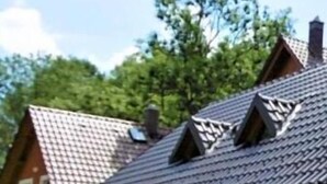 A two-story house with a tiled roof, a brick facade, and a small garden area with shrubs and flowers. - Apartmány Divoký anděl (Dolní Moravice)
