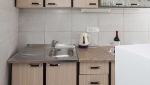 A modern kitchen with light wood cabinets, a stainless steel sink, and a wine glass on the counter. - Apartments Djurkovic (Zupa dubrovacka)