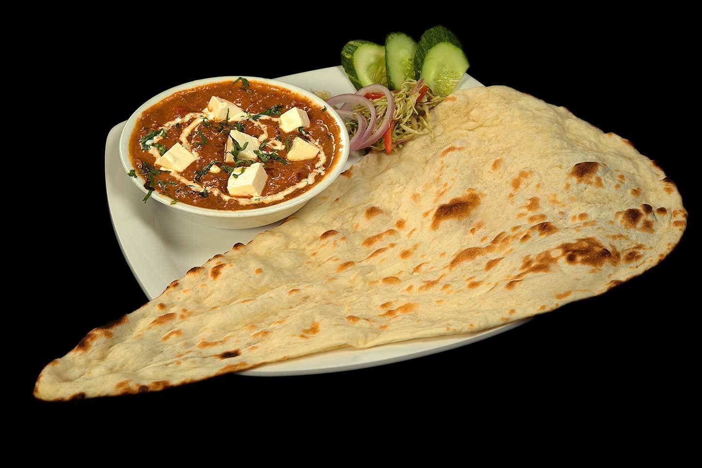 Une assiette avec une galette, un bol de curry et quelques légumes.