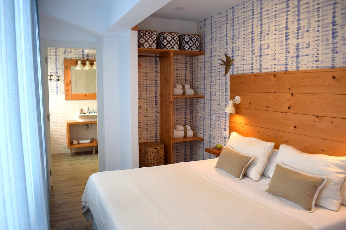A bedroom with a wooden headboard, a large bed with white bedding, and a wooden shelf above the bed holding decorative items.