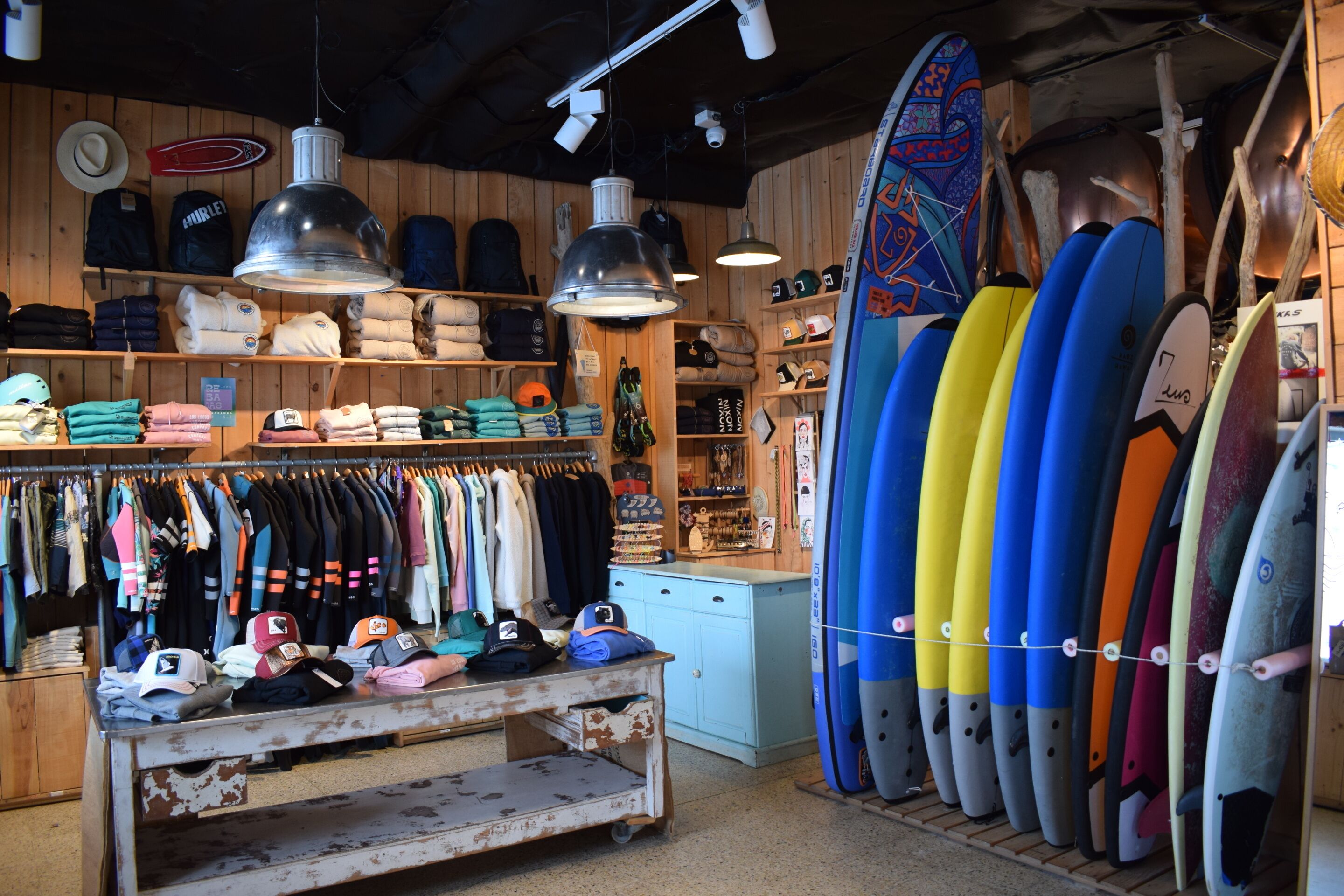 Un magasin de surf où l’on trouve des rangées de planches de surf, des vêtements et des chapeaux.