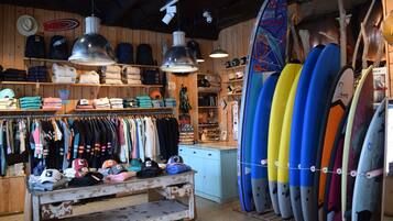 Un magasin de surf où l’on trouve des rangées de planches de surf, des vêtements et des chapeaux.