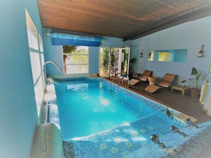Une piscine intérieure à l’eau d’un bleu limpide, avec un sol carrelé et un plafond en bois.