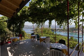 An outdoor terrace with tables and chairs, overlooking a body of water and hills. - Guest House Oreb (Dubrovnik)