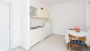 Cocina compacta con armarios blancos, estufa y lavamanos. Hay una mesa de comedor con una silla y un florero con flores.