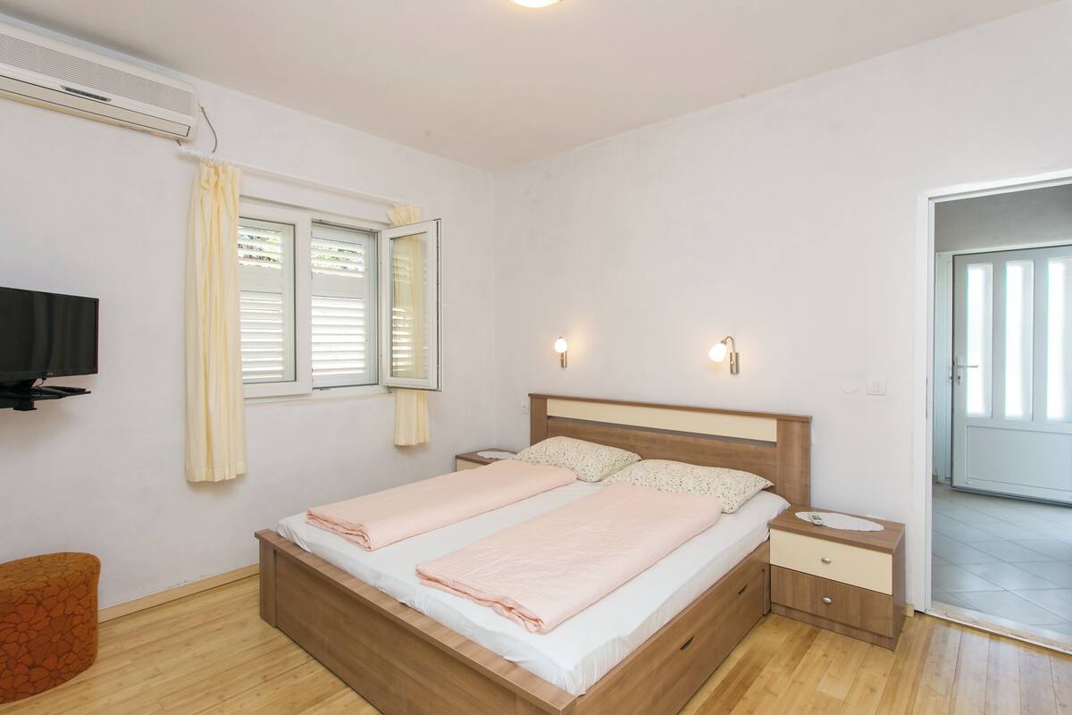 Une chambre à coucher avec un lit en bois, des tables de chevet, une télévision et une fenêtre avec des stores.