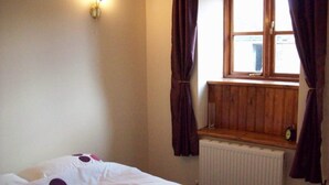 Un dormitorio con una cama individual, una ventana con cortinas, un radiador y una lámpara fijada a la pared.